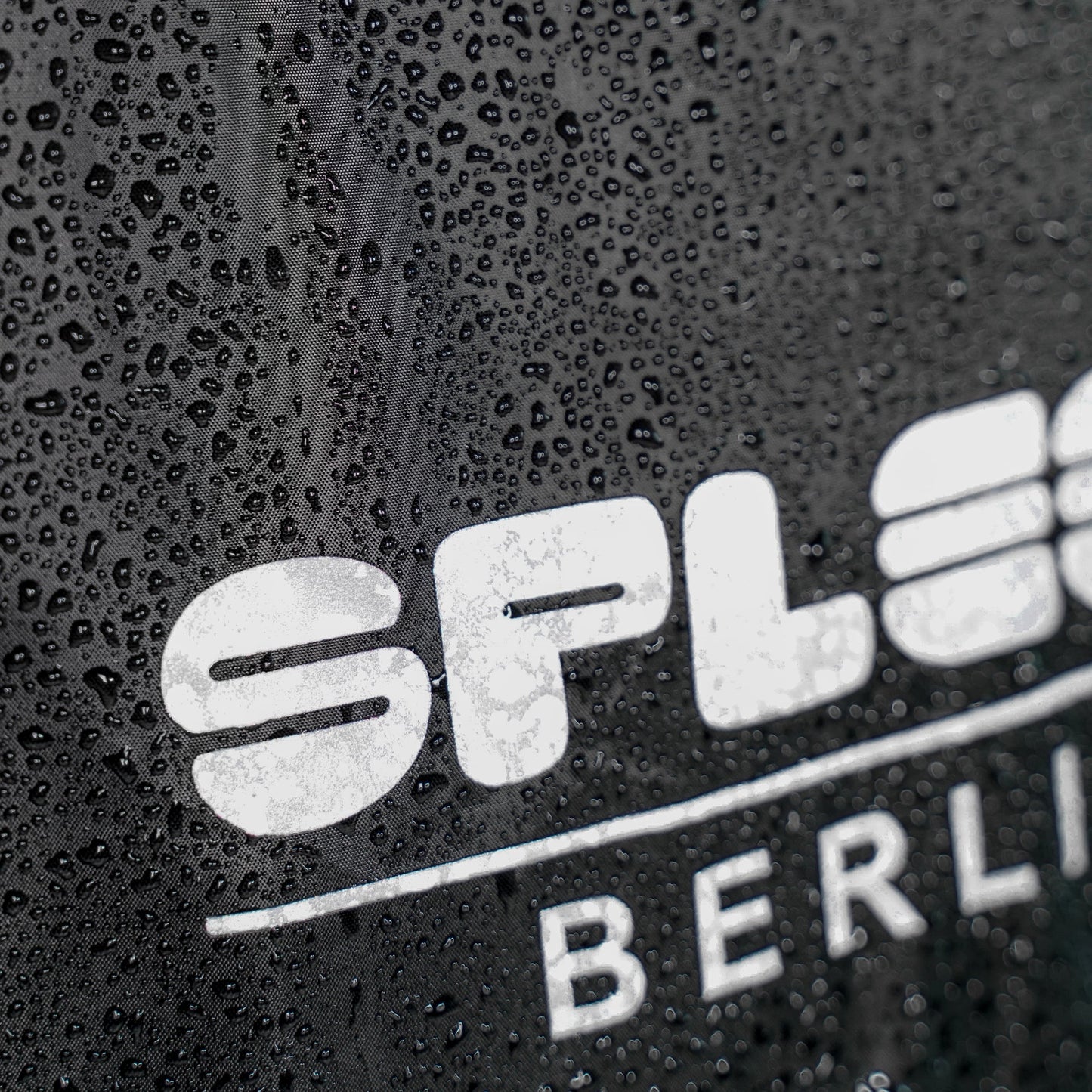 Regencape Schwarz mit reflektierenden Logo von Spleen Berlin, beim Radfahren getragen – optimaler Schutz bei Wind und Wetter.