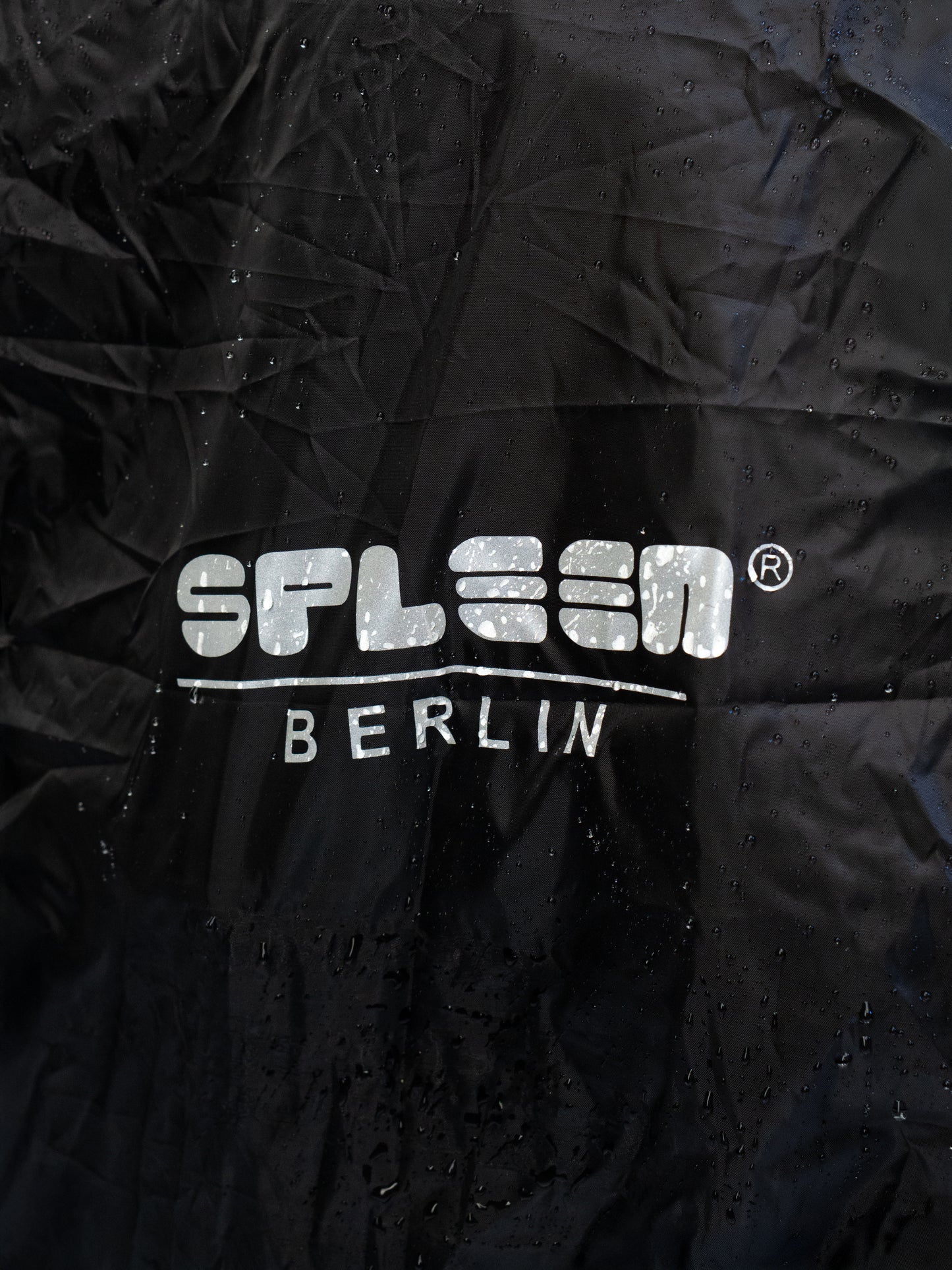 Nahaufnahme Logo Spleen Berlin Aufdruck auf schwarzer wasserdichter Regenhuelle.