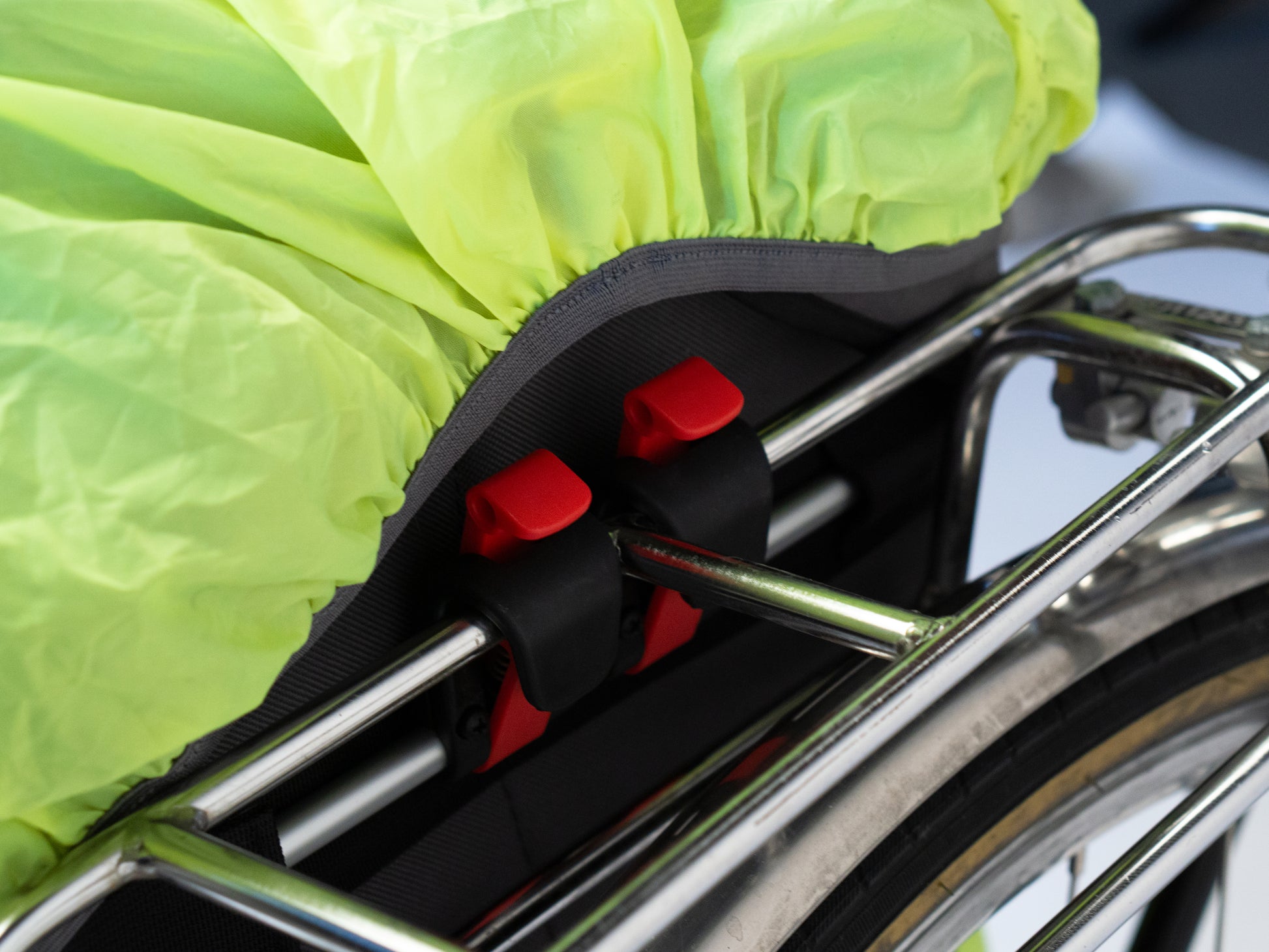 Nahaufnahme, Neongelbe Regnhuelle von Spleen Berlin auf Fahrradtasche am Gepaecktraeger mit rotem Clip.