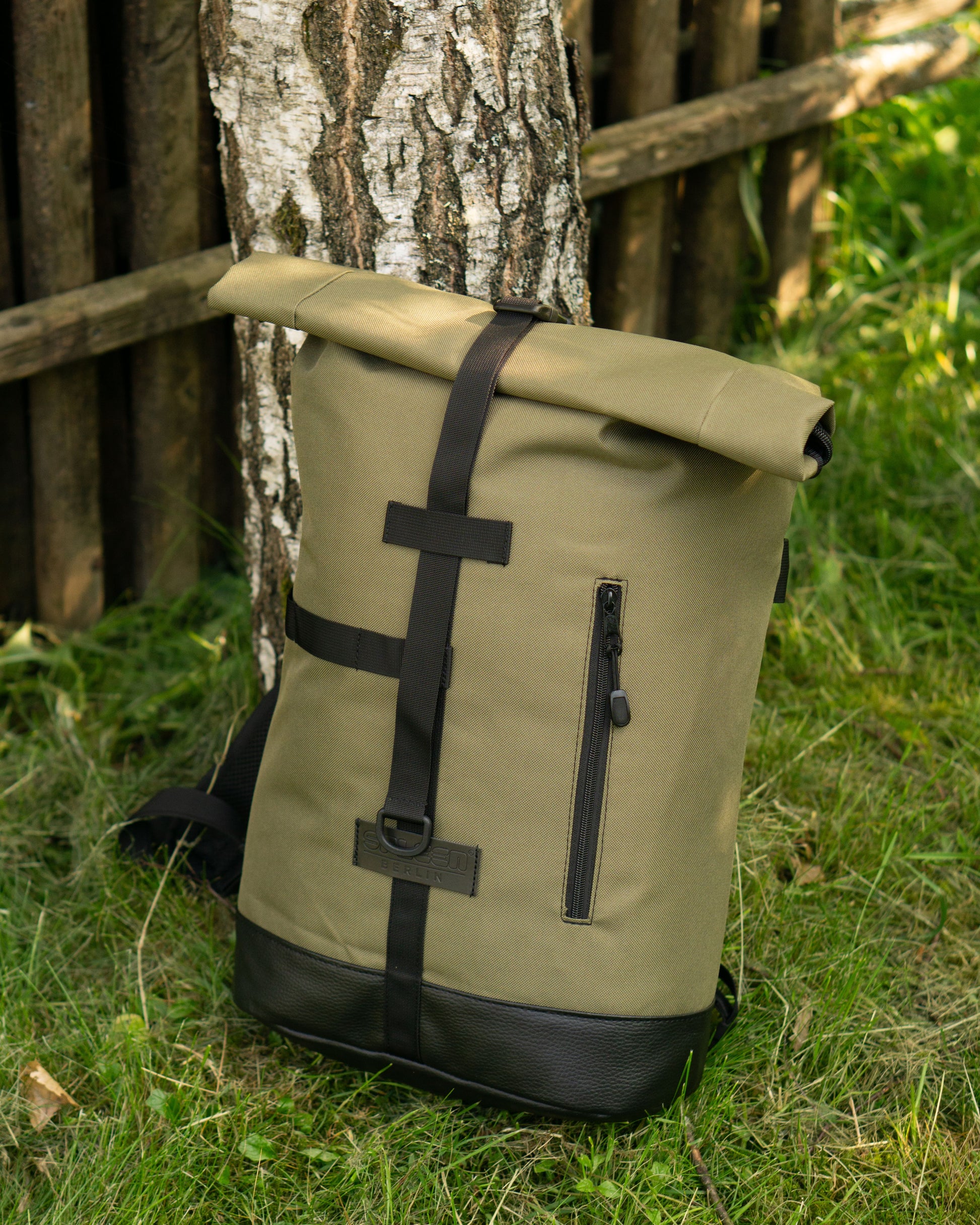 Der•Fixie•Olive•Fahrradrucksack•von•Spleen•Berlin•lehnt•an•einem•Baum•U+2013•bereit•für•die•nächste•Radtour•ins•Grüne.•Der•Rucksack•kombiniert•urbanes•Design mit Funktionalität: mit Fahrradhalterung, viel Stauraum und 
 nachhaltiger Herstellung perfekt für umweltbewusste Abenteurer:innen. ©Spleen Berlin
