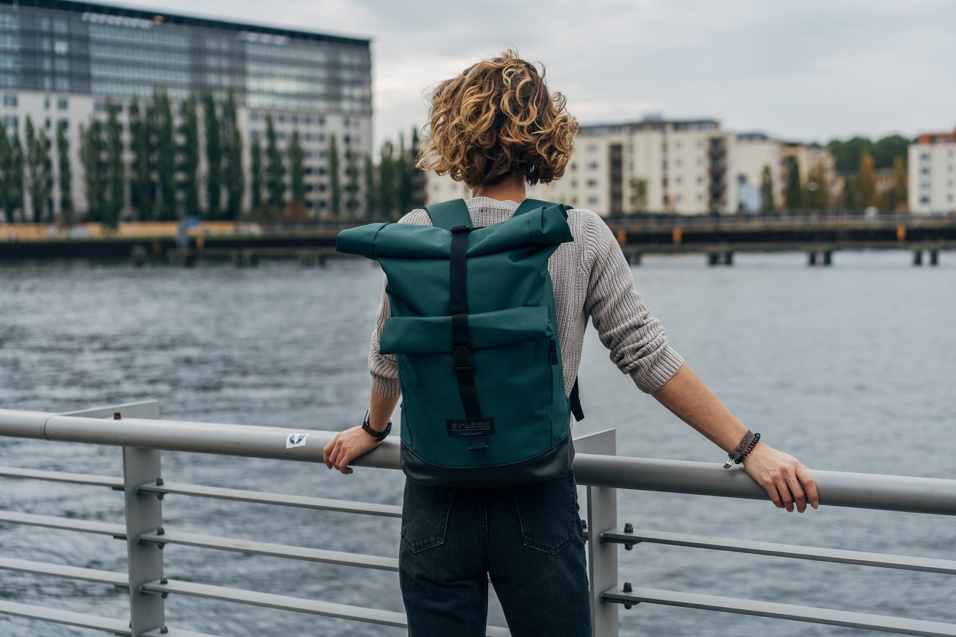 BOB Rucksack British Green von Spleen Berlin getragen von einer Frau die an einem Geländer an der Spree steht, urbaner Look, Fahrradrucksack & Fahrradtasche. ©Spleen Berlin
