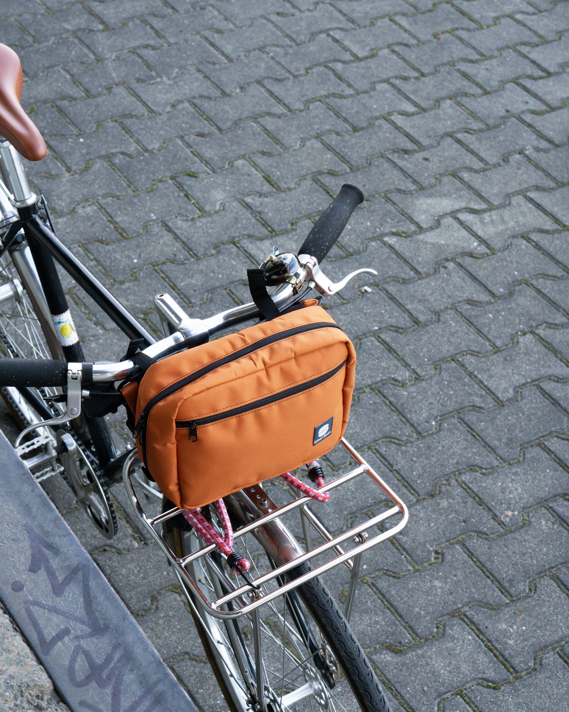 Crossbody & Lenkertasche Skandinavian-Orange von Spleen Berlin – leuchtende, wasserabweisende 2-in-1 Tasche (3,5 l) am Fahrradlenker befestigt. 
@Spleen Berlin