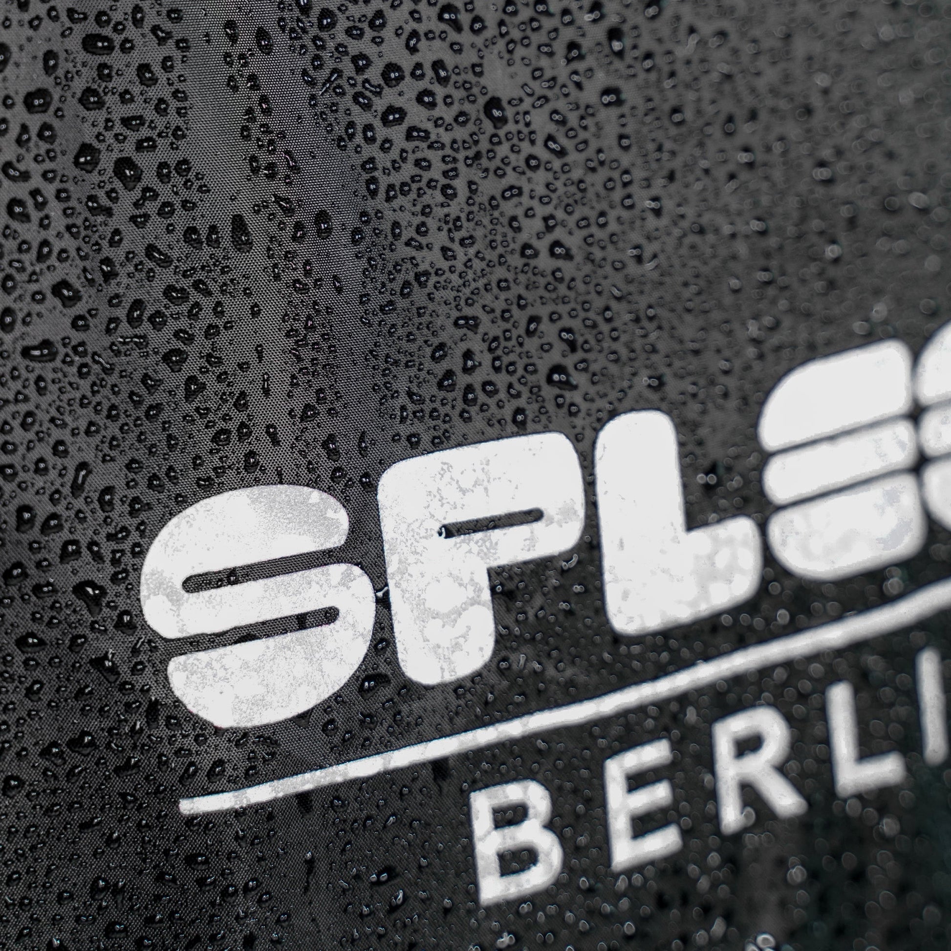 Regencape Schwarz mit reflektierenden Logo von Spleen Berlin, beim Radfahren getragen – optimaler Schutz bei Wind und Wetter.