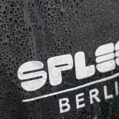 Regencape Schwarz mit reflektierenden Logo von Spleen Berlin, beim Radfahren getragen – optimaler Schutz bei Wind und Wetter.