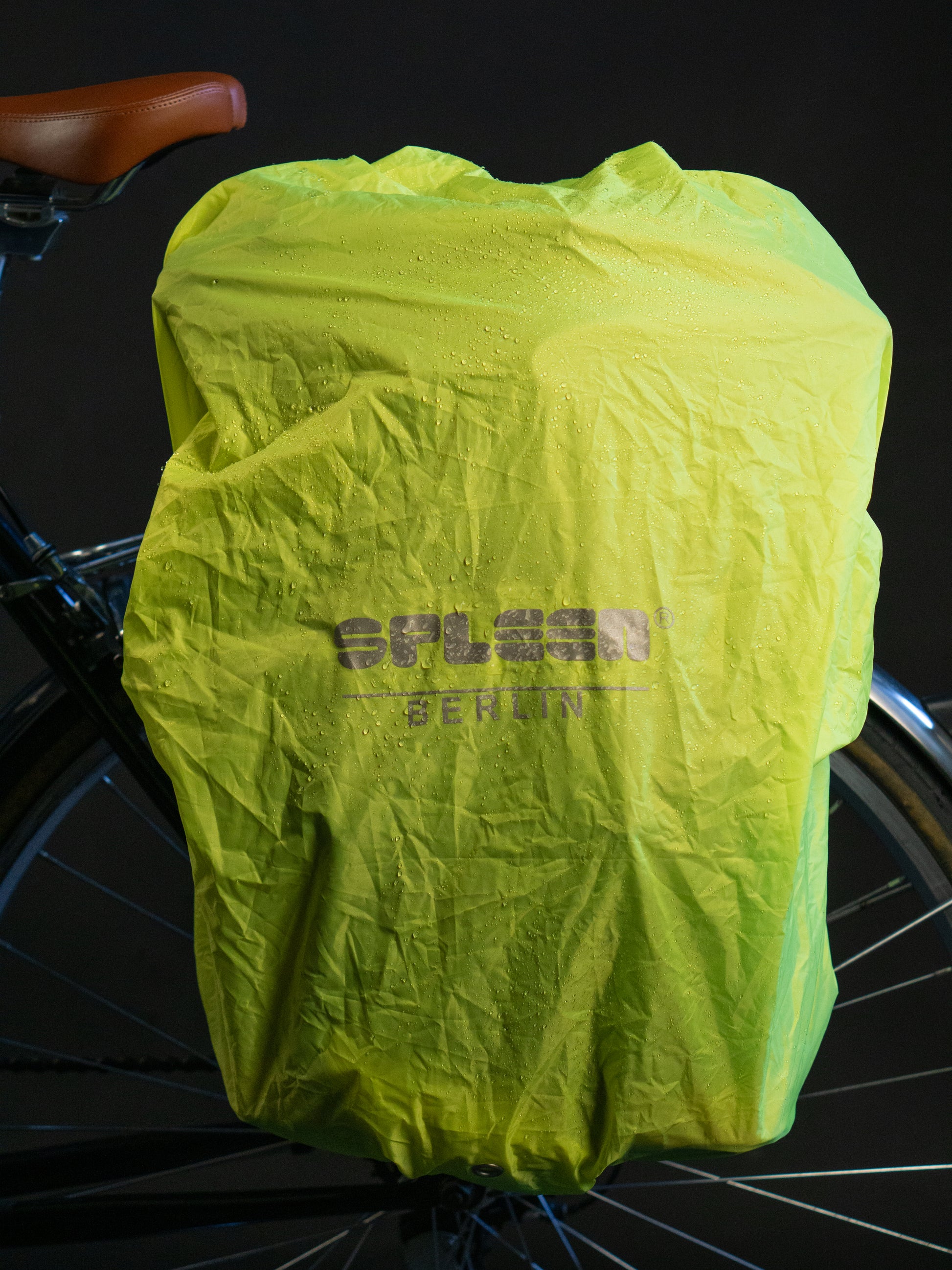 Neongelber wasserdichter Regenschutz von Spleen Berlin für Fahrradrucksäcke  mit 30l Volumen am Fahrrad befestigt bei Nacht.