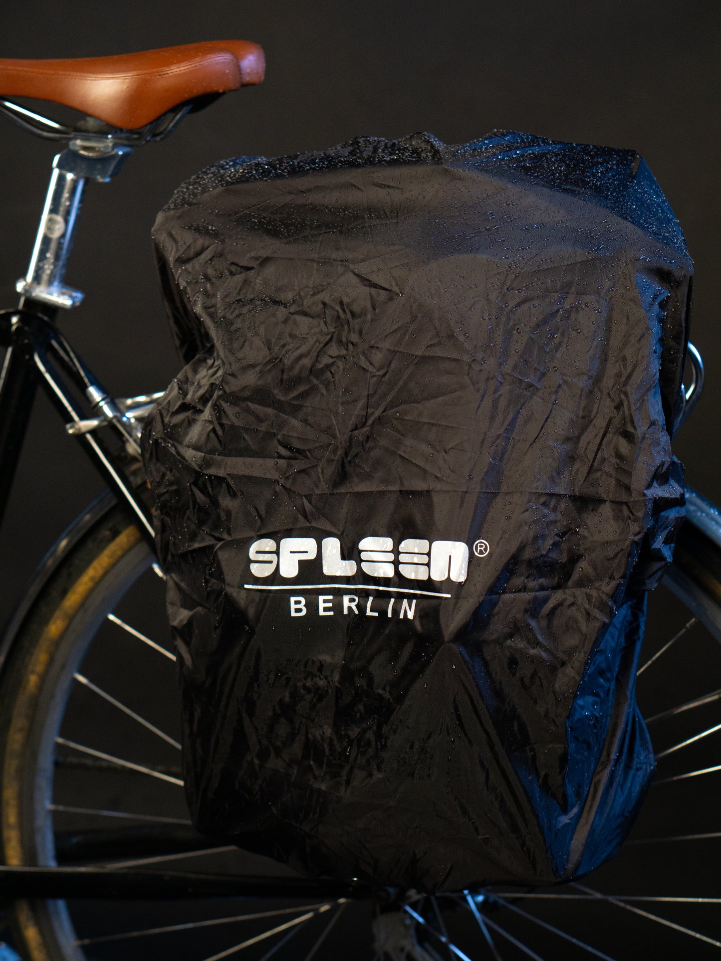 Regenhuelle in schwarz mit reflektierendem Aufdruck von Spleen Berlin befestigt am Fahrrad  bei Nacht.